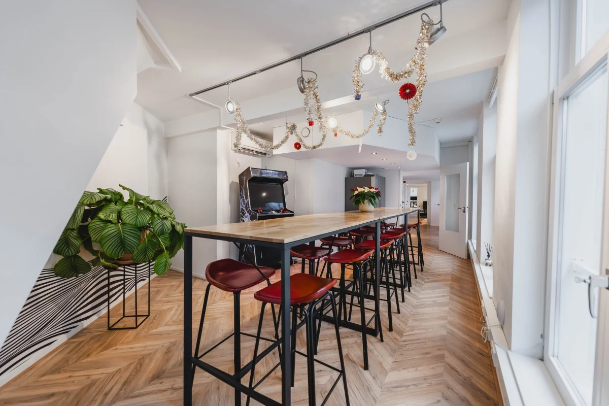 Moderne en sfeervol ingerichte gemeenschappelijke ruimte in de Korte Reguliersdwarsstraat met hoge tafel, barkrukken, planten, een arcadekast en feestversiering.